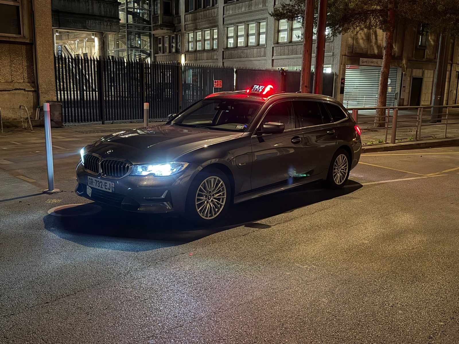 Taxi BMW 320e avec lumineux allumé devant la gare SNCF d'Amiens la nuit